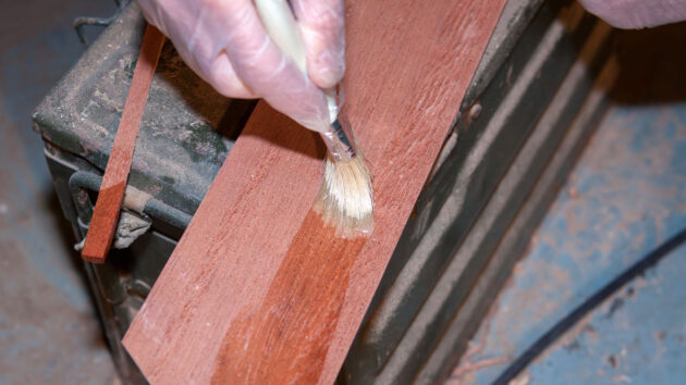 A man painting epoxy onto a piece of wood during the cold moulding process of boat building