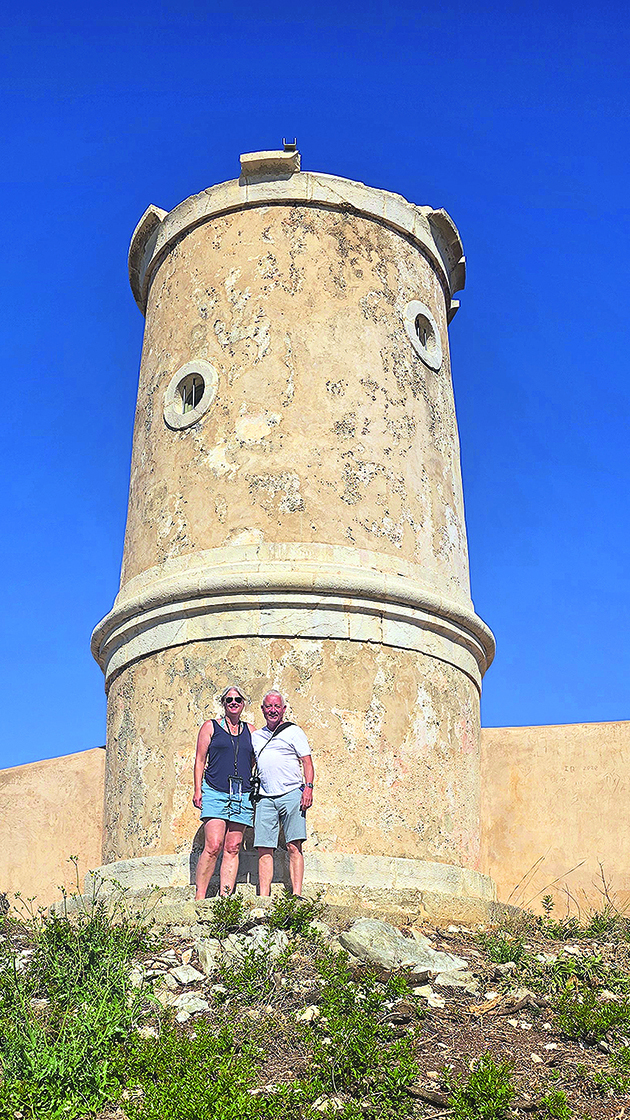 A woman and man standing by an old lighthouse on a Greek island