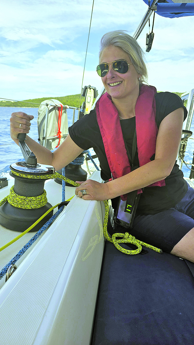 A woman wearing a lifejacket using a winch on a boat to control the sails while on a charter holiday in Greece