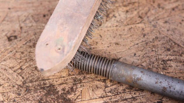A brush being used to clean a keel bolt for a boat