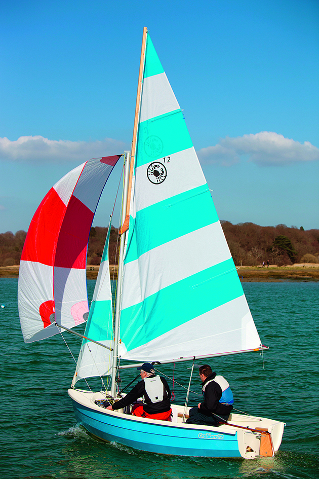 two people sailing a Cornish Crabber 12 with blue and white sails