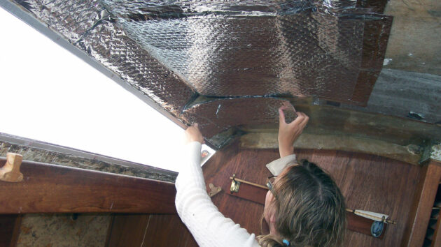 A woman applying tin foil bubble wrap for insulation on her boat