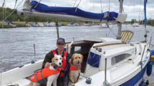 A man sitting on a boat with two dogs.