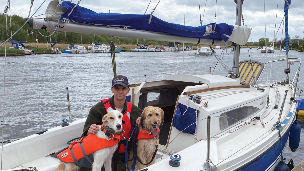A man sitting on a boat with two dogs.