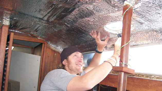 A man trimming bubble wrap which is being fitted to the ceiling of a boat cabin for insulation