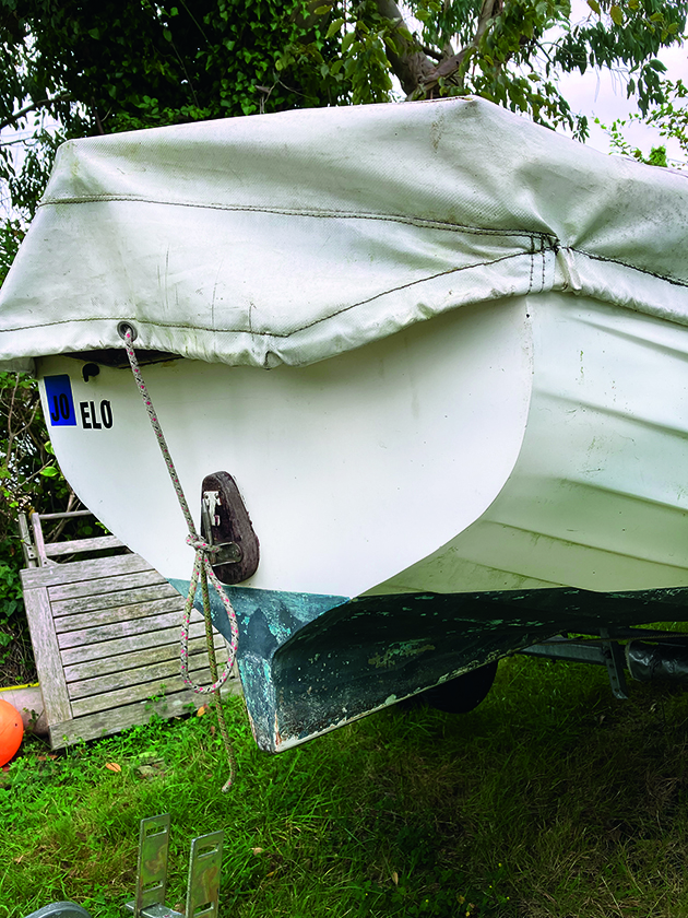 A boat on a trailer on a lawn covered with a tarp