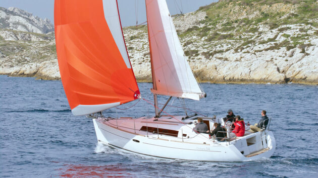 A yacht with a red sail sailing along the coast