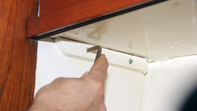 A person using an offset screwdriver on a boat, one of many tools for tight spaces to have on board