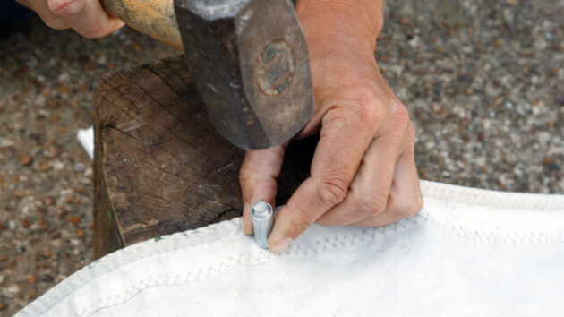 A man adding an eyelet to a sail 