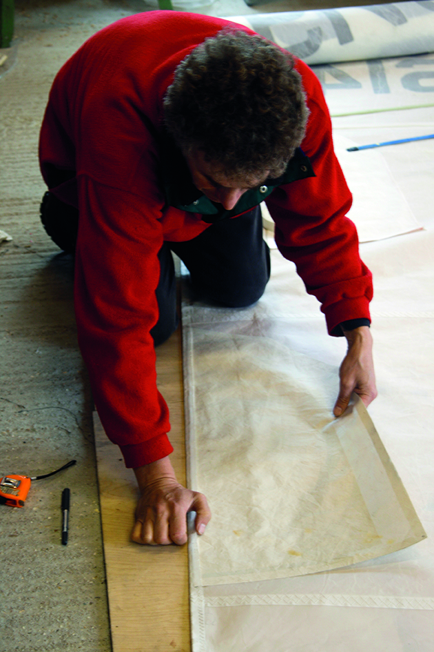 A man reinforcing sails for reefing points