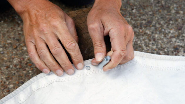 A man fitting an eyelet to a sail