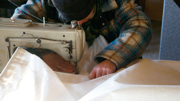 A person sewing sail cloth with a sewing machine