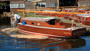 A man pushing sawdust around a boat to help stem leaks on a wooden boat
