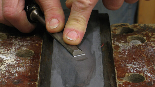 A man showing how to sharpen a chisel on an oilstone