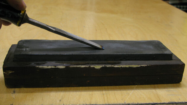 A chisel being ground on a oilstone