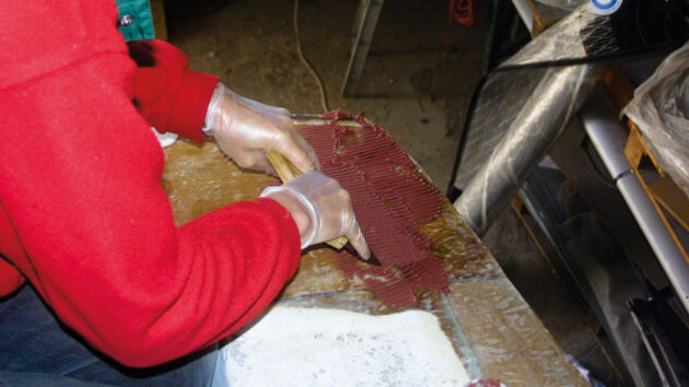 A man using a notched spreader to apply fairing compound to a boat