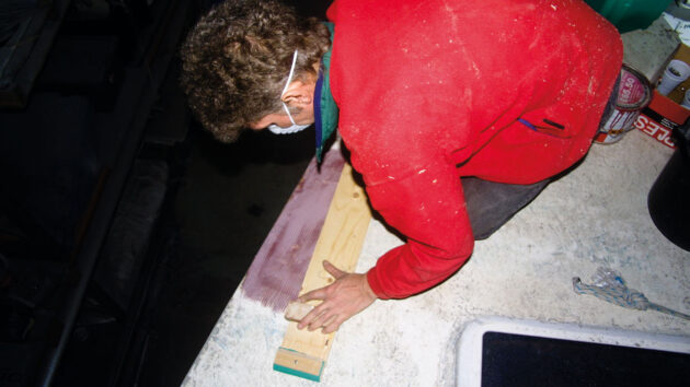 A man using a longboard to sand fairing compound on plywood decks