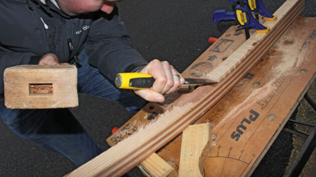 A man using a chisel to shape a new tiller for a boat