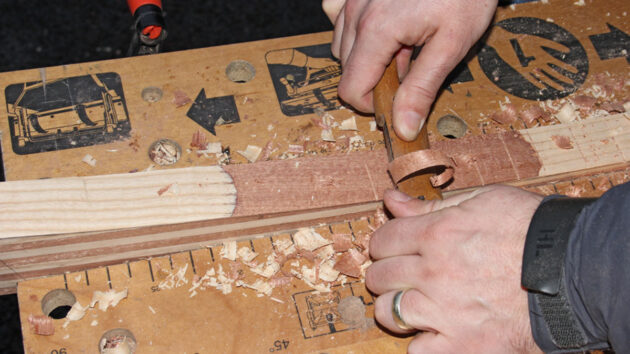 A man shaving wood to make a tiller for a boat