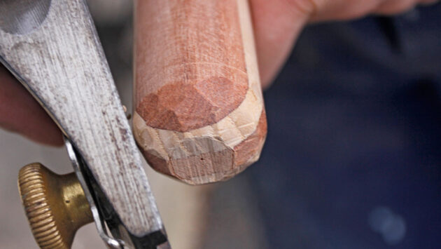 A man using a block plane for shaping a tiller for a boat
