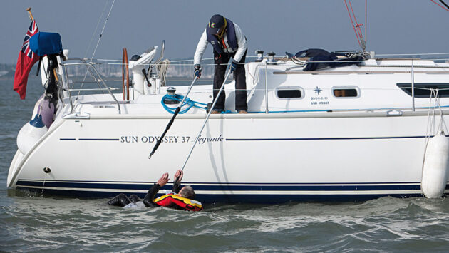 A woman passing a boat hook to a man in the water as part of MOB recovery