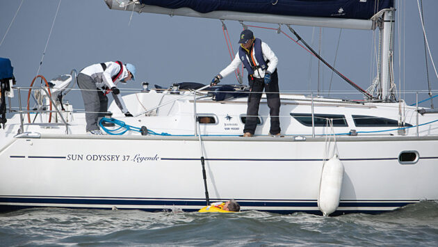 Two people preparing to winch a man onboard a boat