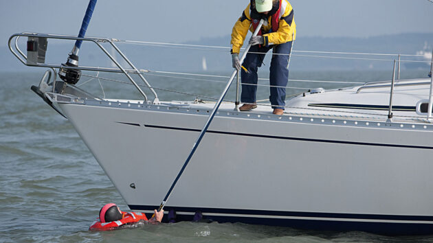 A sailor using a pole to help recover a man overboard a yacht