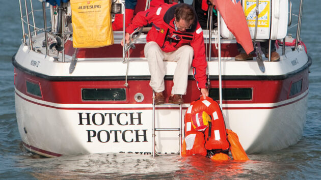 A man holding onto a man in the water via his lifejacket as part of MOB recovery