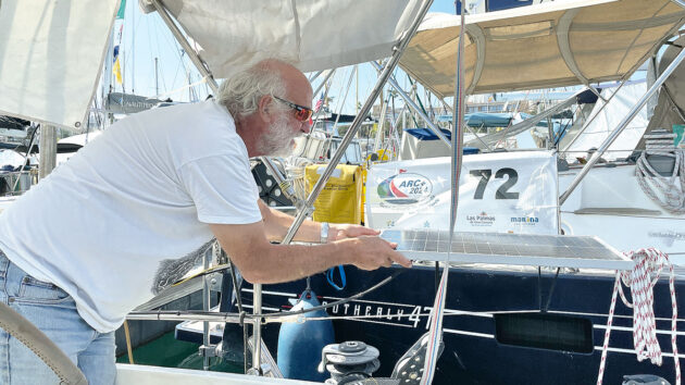 A man with a beard adjusting a solar panel on the side of his boat