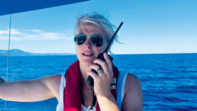 A woman talking on a VHF radio on a boat. It is an important part of the ColRegs to communicate with other vessels