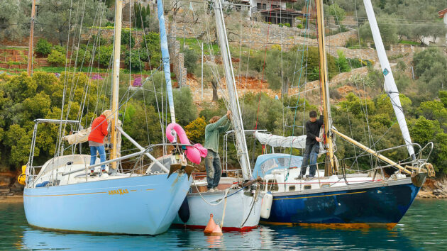 Three people preparing to unstep a mast of a yacht