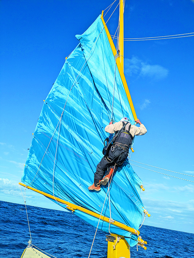 Pete Hill up the mast of his junk-rigged catamaran in the middle of the ocean