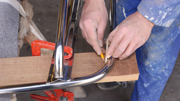 A man measuring to screw wood planks into a stainless steel frame to make a boat swimming platform
