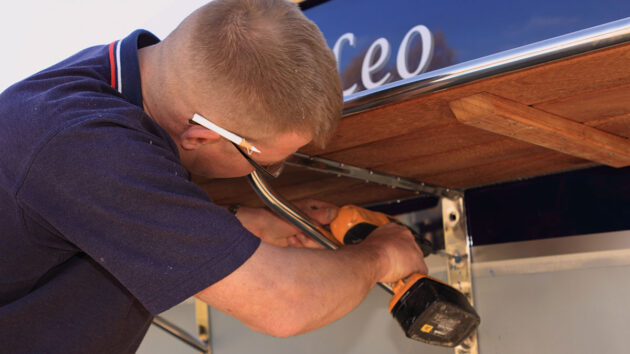 A man drilling holes in a boat to fit a boat swimming platform