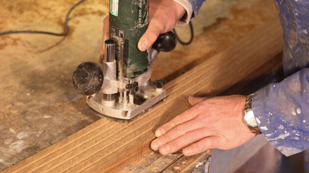 A man using a router to bevel the edge of wood planks to build a boat swimming platform