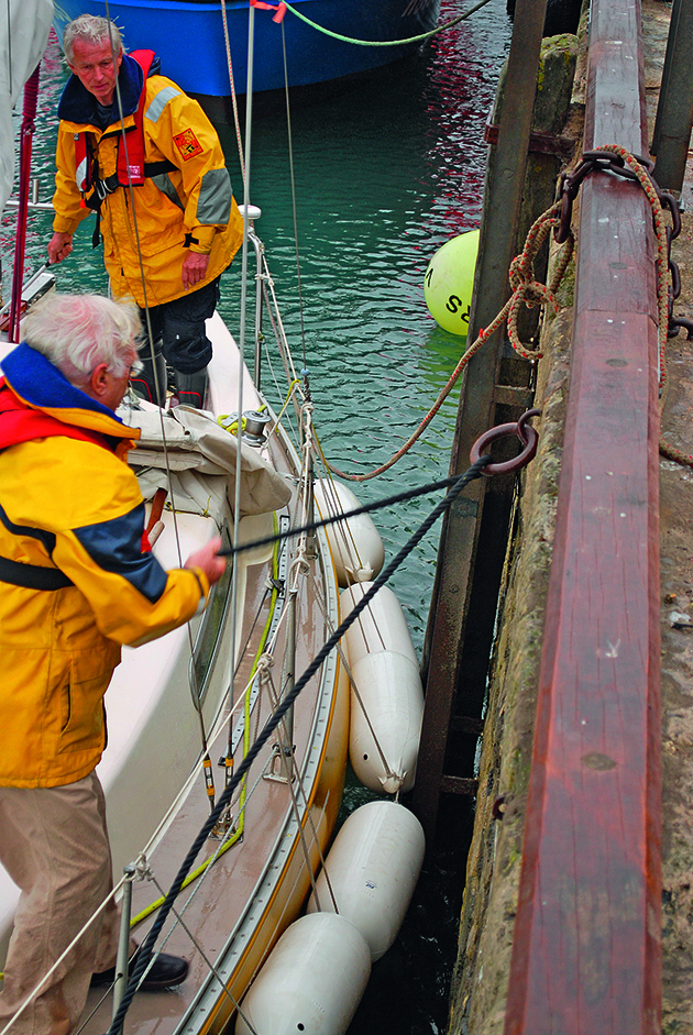 A man using a rope to tie a boat to a harbour wall