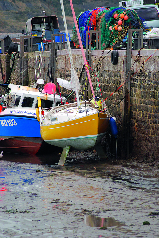 a yacht with a yellow hull tied up against a wall in a harbour