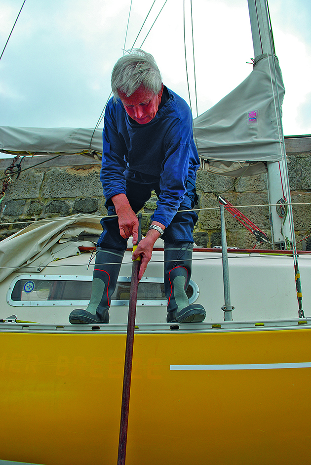 A man using a boat hook to check the depth while drying out a boat against a harbour wall