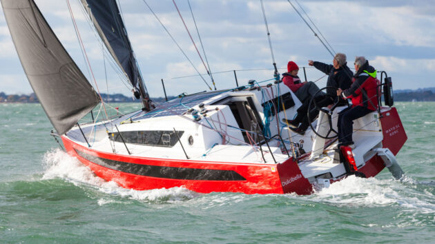A red hulled yacht with black sails being sailed