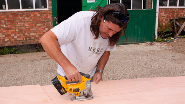 A man cutting plywood veneer with a jigsaw hand tool
