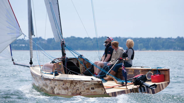 Three people sailing a small yacht with white sails