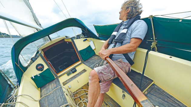 A man holding onto a rudder while battling weather helm on a boat