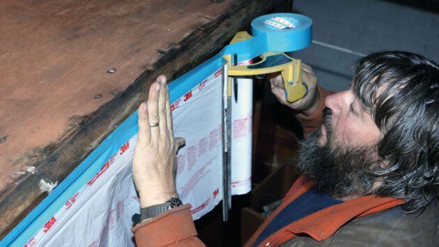 A man masking off part of a boat coachroof before epoxy sheathing
