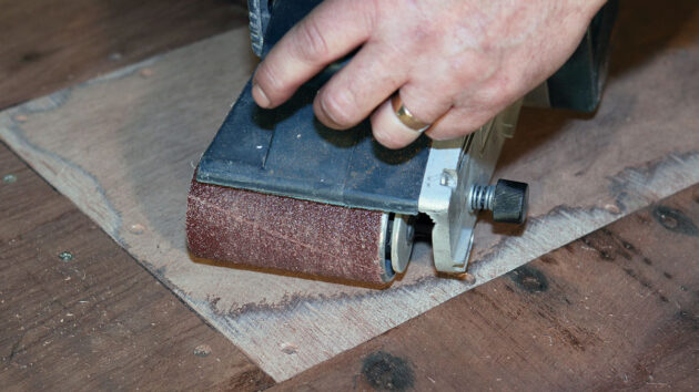 A belt sander being used on wood on a boat