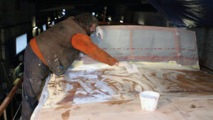 Two men epoxy sheathing the coachroof of a motor boat