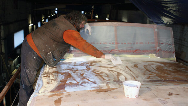 Two men epoxy sheathing the coachroof of a motor boat