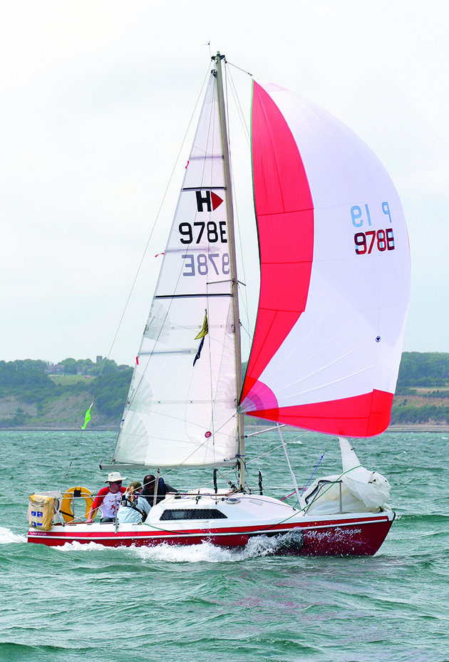 A boat with a masthead rig and red and white sails sailing