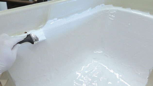 A person painting gel coat on a bath to make a mould for a doghouse for a boat
