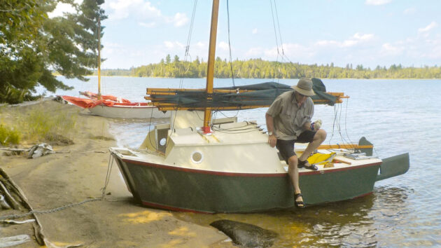 A man climbing out of a trailer-sailer which has been beached