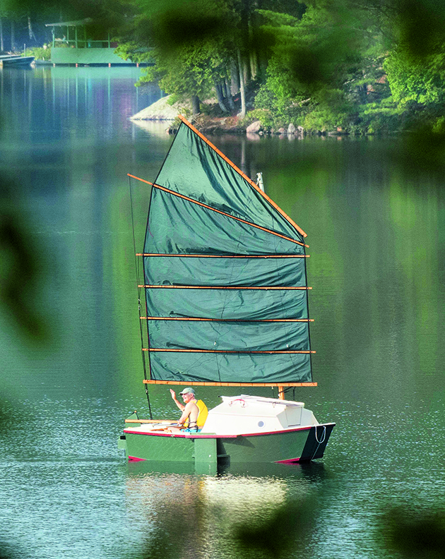 A man sailing a small trailer-sailer with a junk rig sail on a lake